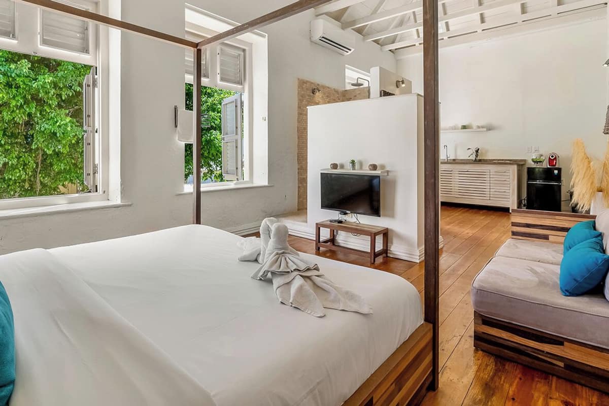 Une chambre avec un grand lit, une télévision, un plancher en bois et une vue sur la verdure.