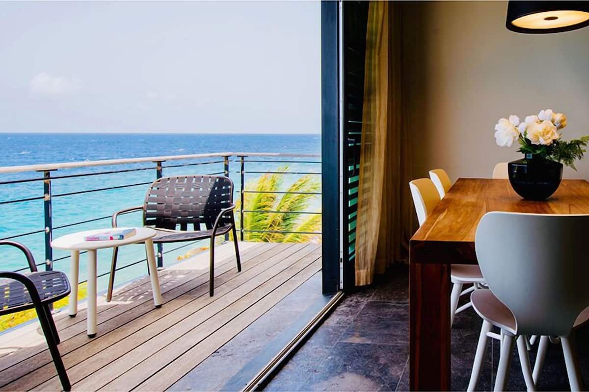 A balcony with a view of the sea, a dining area with a table and chairs, and a vase with flowers.