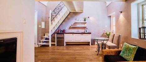 Una sala de estar acogedora con chimenea, un comedor con mesa y sillas, una cocina con escalera, y un sofá con cojines.