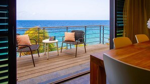 Un balcon doté d’un plancher en bois, de deux chaises, d’une petite table ronde et offrant une vue sur l’océan.