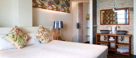 A hotel room with a large bed, a nightstand with a lamp, a bathroom with a stone sink and a mirror.