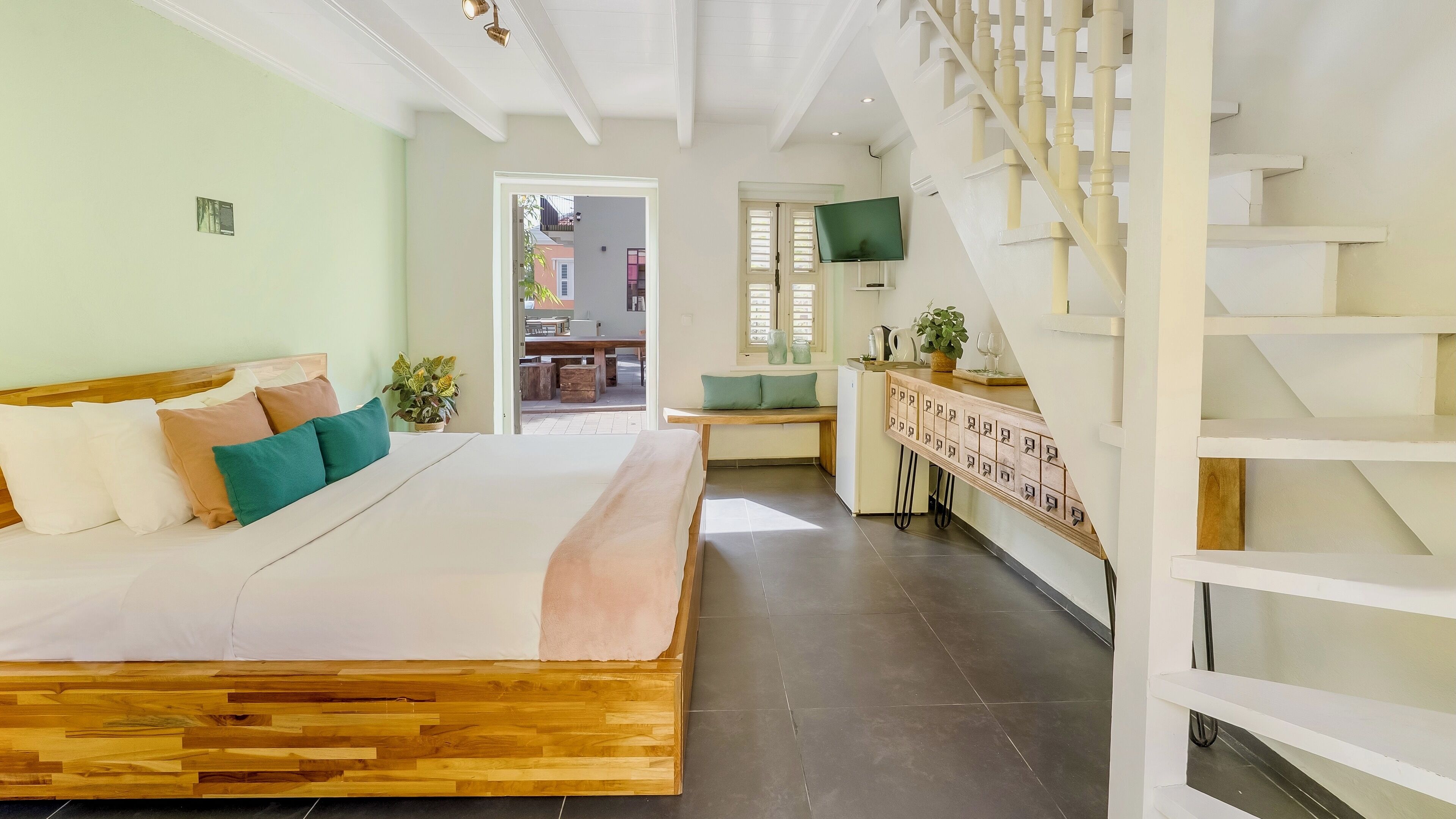 A bedroom with a wooden bed, a bench, a TV, and a staircase.
