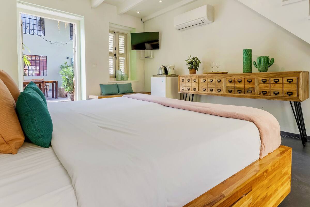 A modern bedroom with a large bed, a wooden nightstand, a TV, and a small kitchenette.