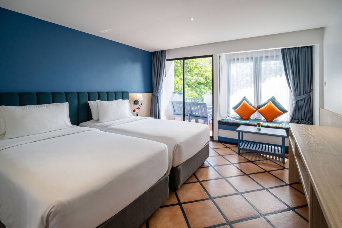 A hotel room with two beds, a small table, and a view of the outdoors.