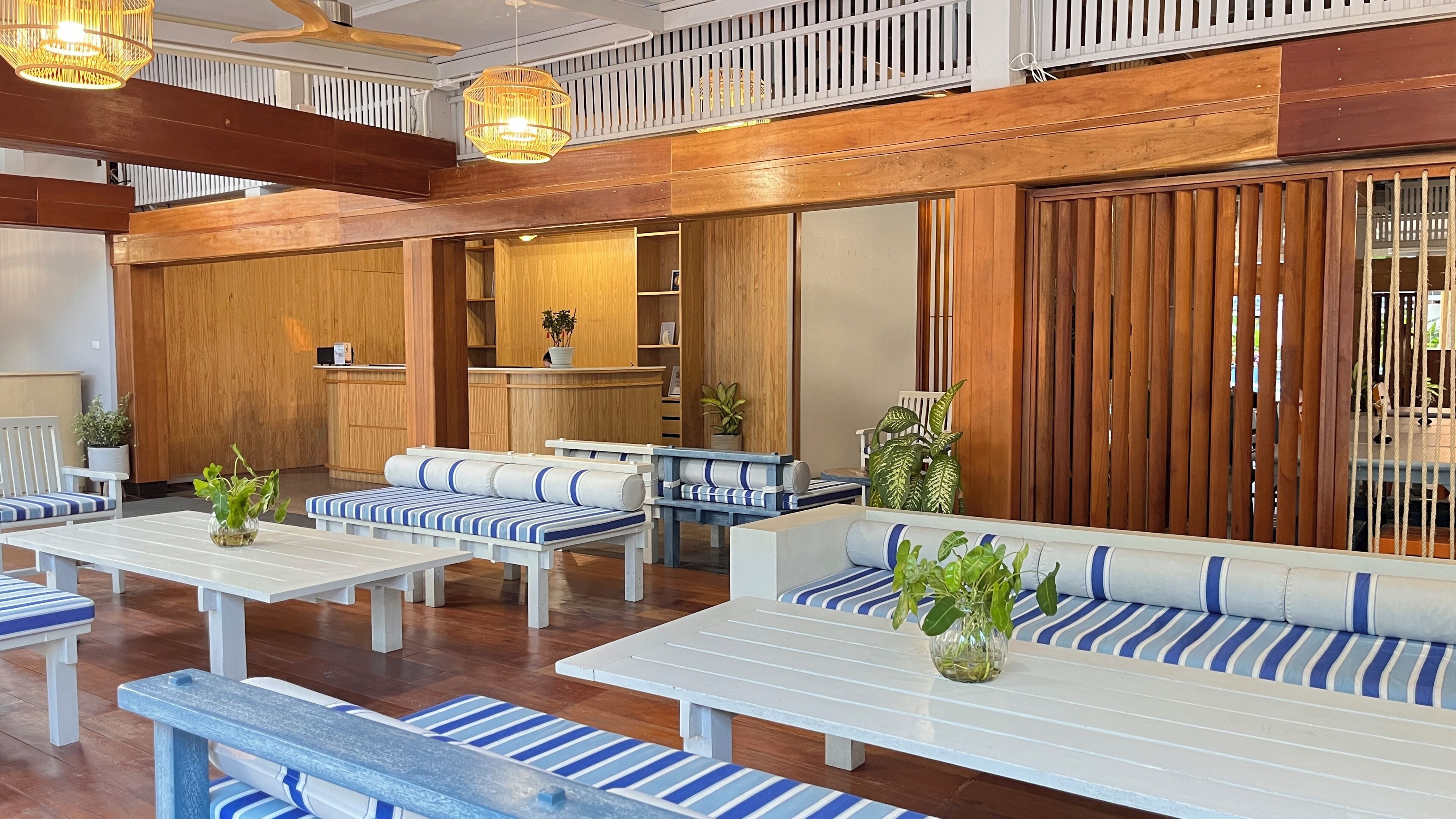 A hotel lobby with wooden paneling, white benches with blue stripes, and hanging wicker lamps.