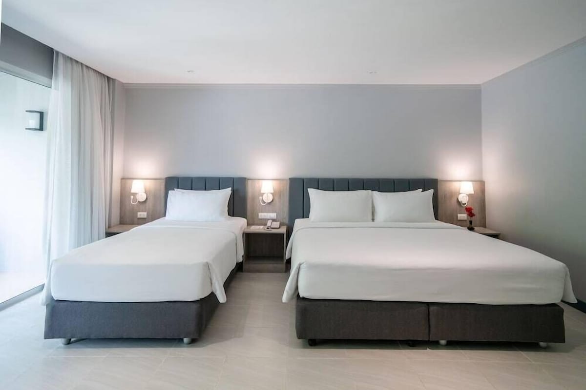 A hotel room with two beds, nightstands, bedside lamps, and a window with curtains.