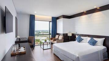 A modern hotel room with a large bed, a desk, a chair, and a view of the city.
