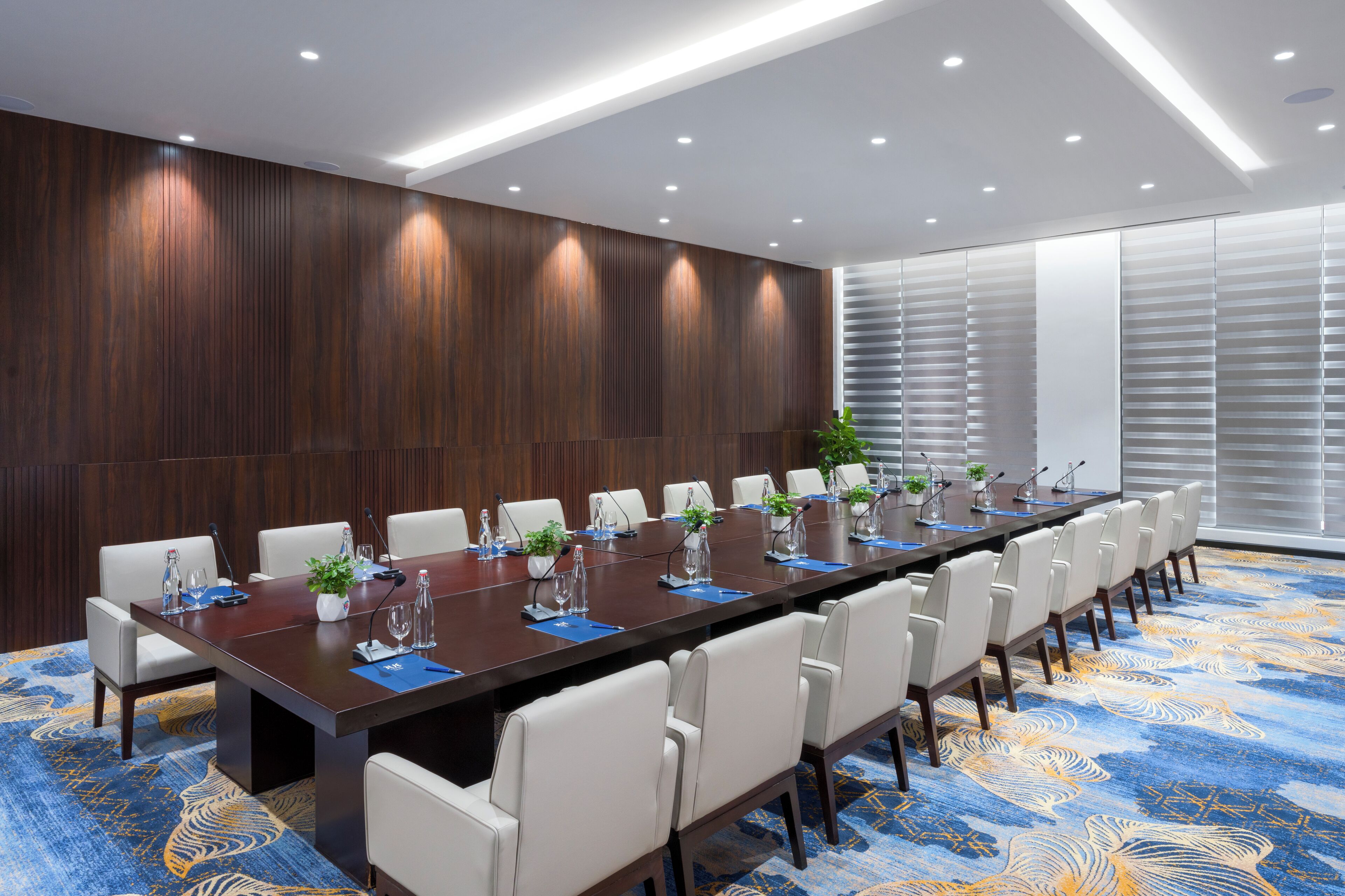 A conference room with a long table, white chairs, and a blue patterned carpet.