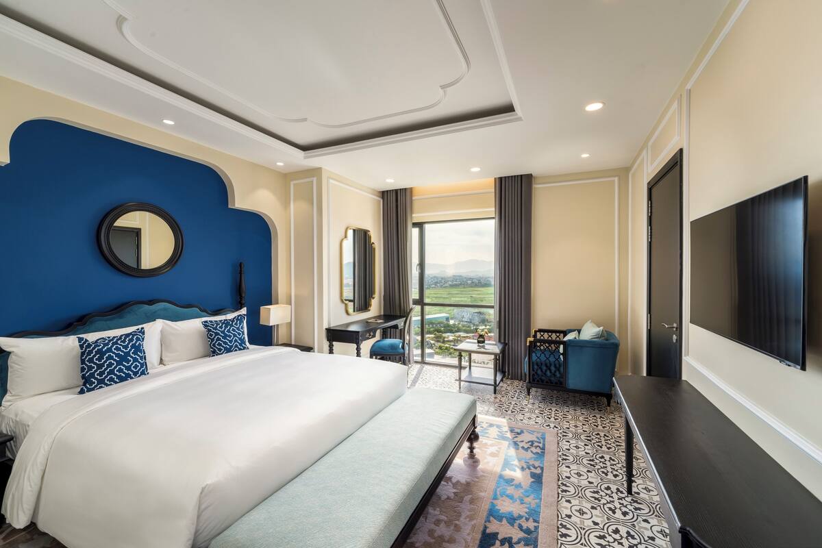 Een ruime hotelkamer met een groot bed, een bureau, een televisie en uitzicht op de omgeving.