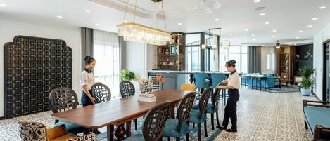 A hotel dining area with a long wooden table, blue upholstered chairs, and a chandelier.