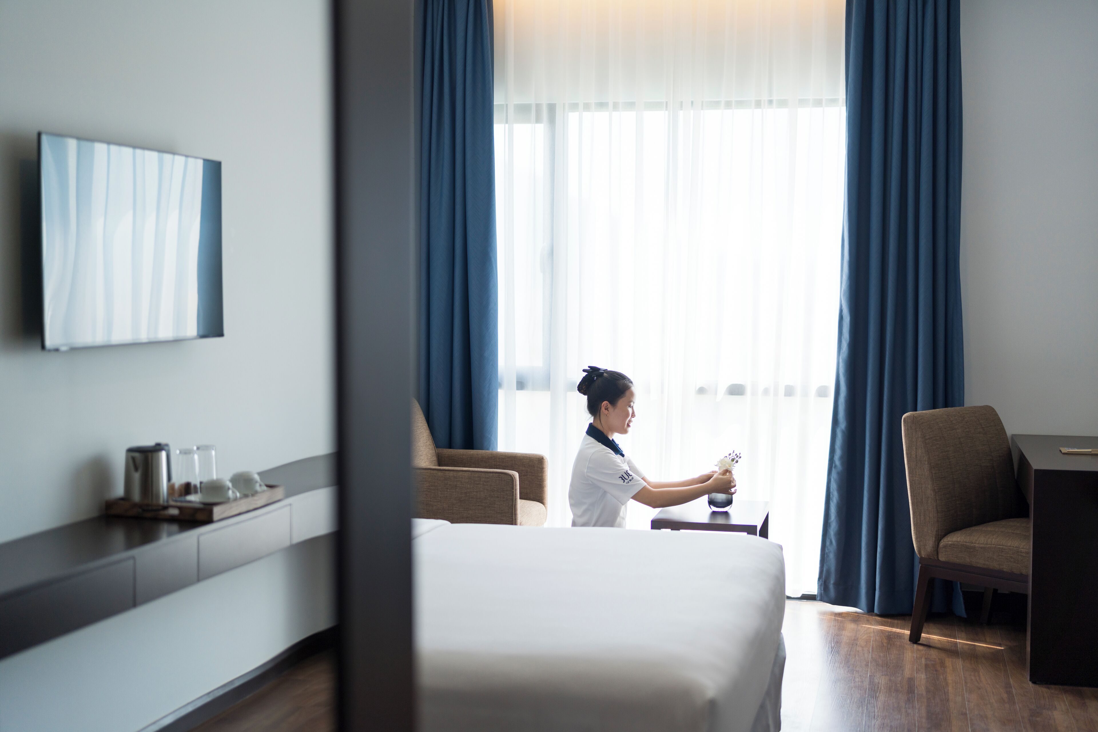 A hotel room with a bed, a desk, a chair, and a large window with curtains.