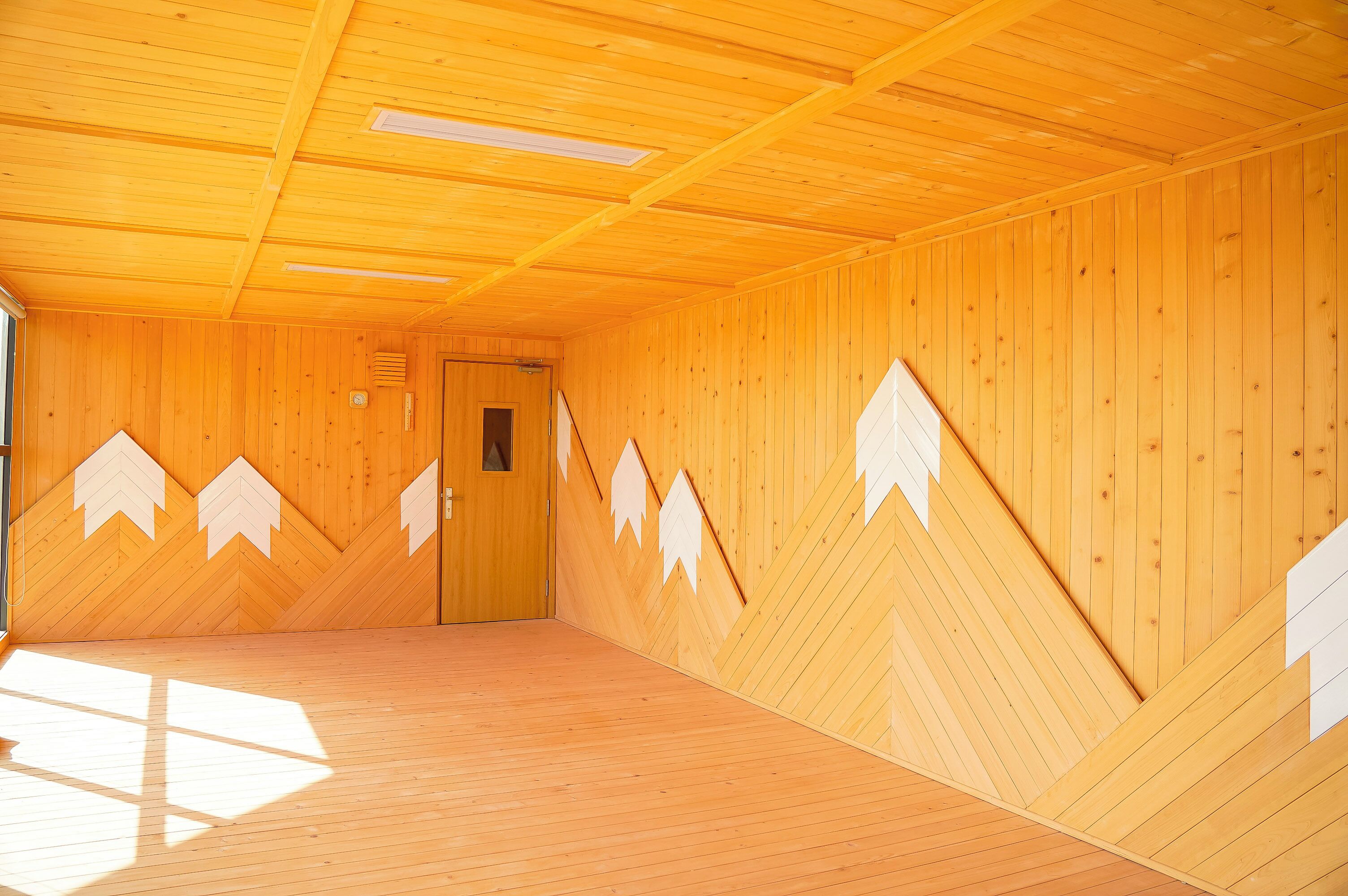Une pièce aux murs et au plafond en bois, avec une porte et une fenêtre laissant entrer la lumière naturelle.