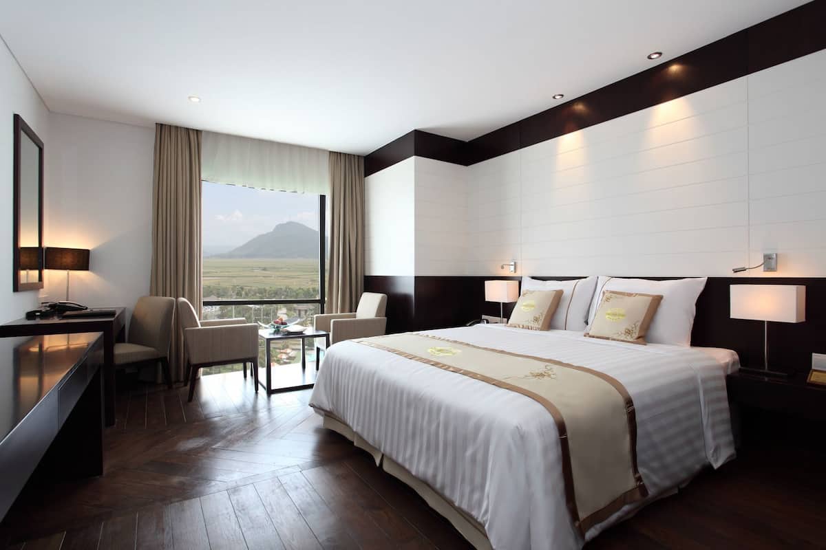 Een hotelkamer met een groot bed, een bureau, een stoel, een tafel en uitzicht op een berg.