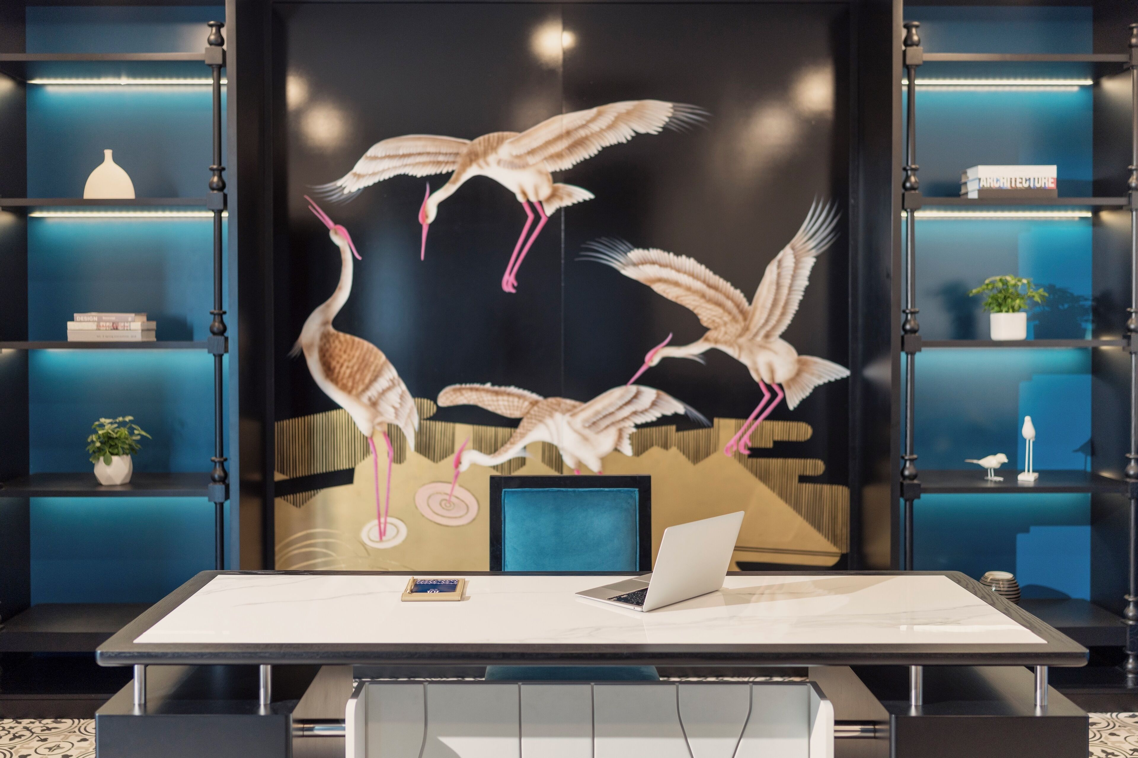 A modern office space with a desk, laptop, and a wall mural of cranes.