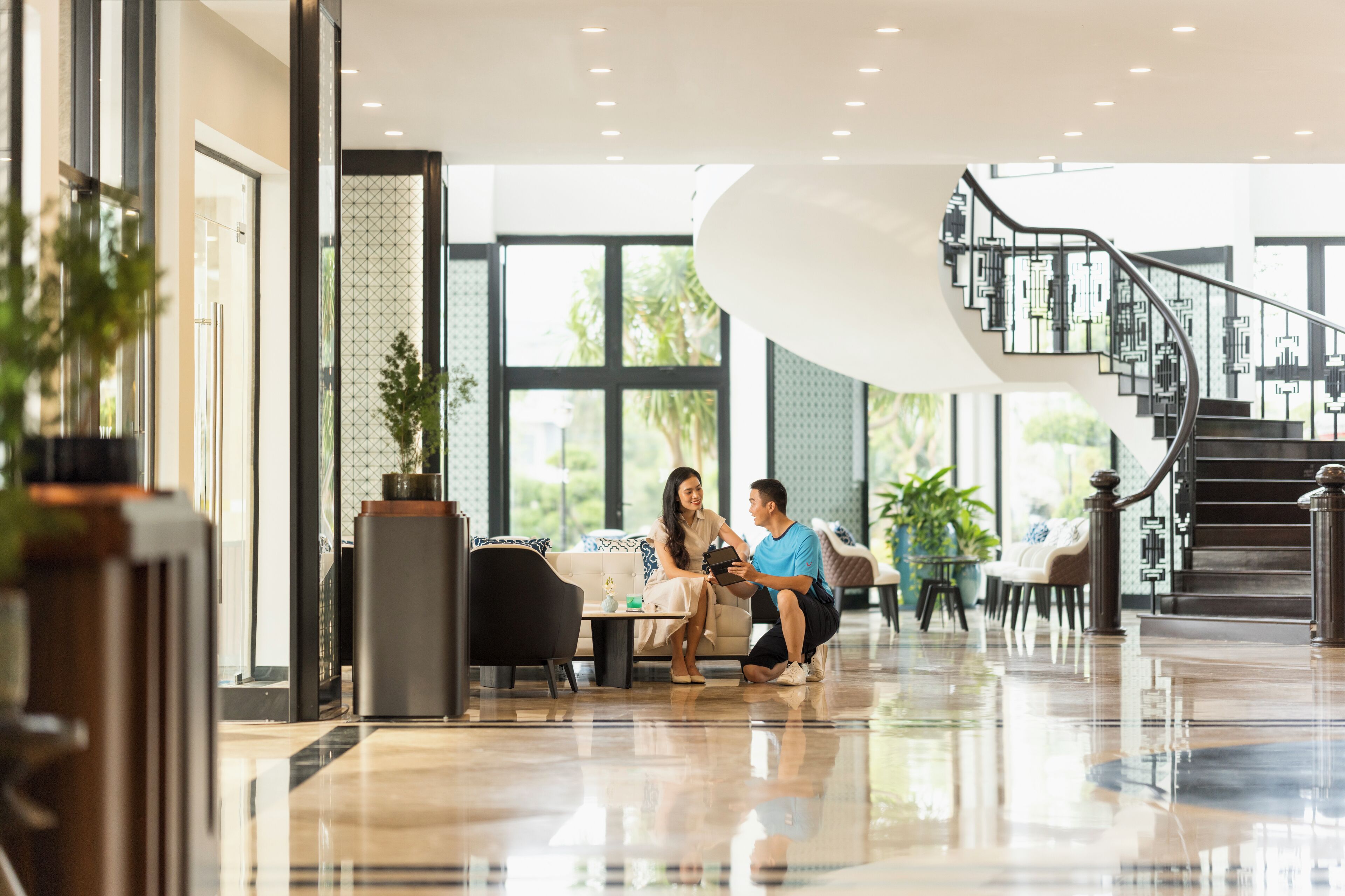 A spacious lobby with a modern staircase, a seating area, and large windows.