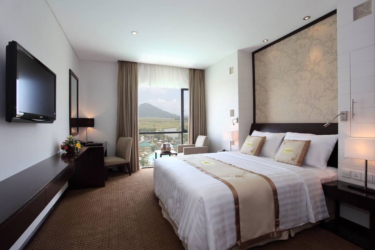 Een hotelkamer met een bed, een televisie, een bureau, een stoel en uitzicht op het omliggende landschap.