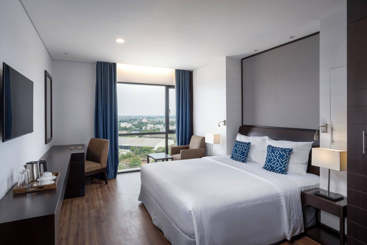 Een moderne hotelkamer met een groot bed, een bureau, een stoel en uitzicht op de stad door het raam.