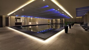 Una piscina interior moderna amb un disseny de sostre geomètric, una zona de recepció i plantes en testos.