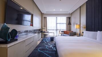 A hotel room with a large bed, a desk with a chair, a television, and a window with curtains.