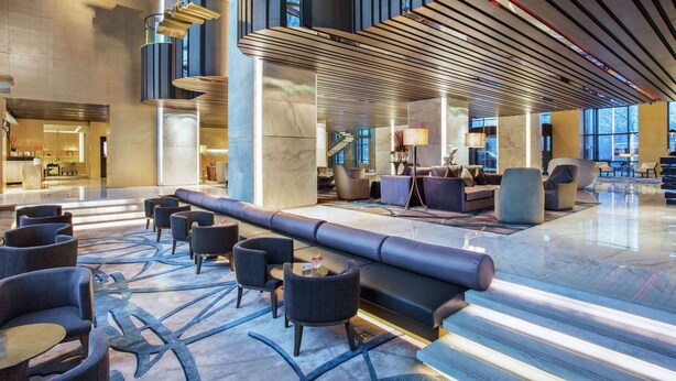 Een ruime lobby met een lange bank, zithoek en moderne verlichting.