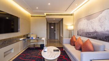 A modern hotel room with a sofa, a coffee table, a TV, and a large painting on the wall.