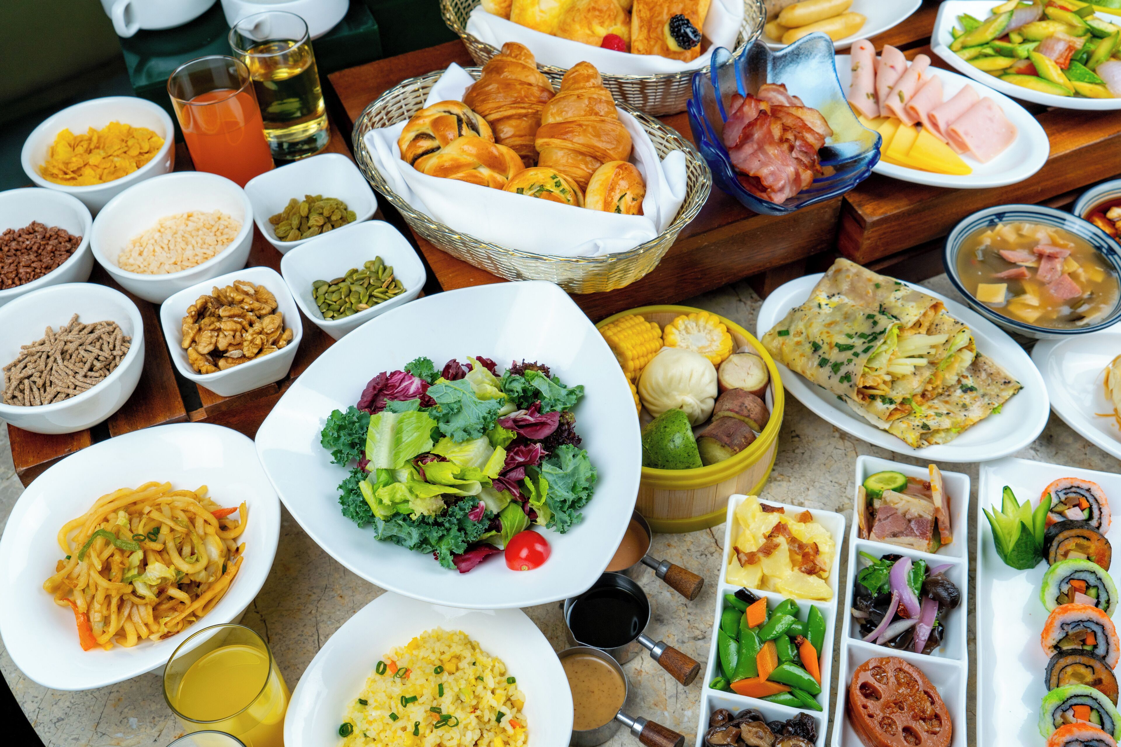 Une variété d’aliments sont disposés sur une table, notamment des salades, des pâtisseries et des sushis.