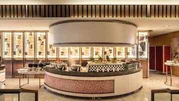 A hotel lobby with a central reception desk, a patterned wall, and a large window with geometric designs.