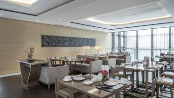 A modern dining area with multiple tables and chairs, a large window providing natural light, and a wall with abstract art.