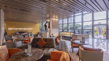 Un área de estar moderna con asientos cómodos, un bar y ventanas amplias que ofrecen vistas a la ciudad.