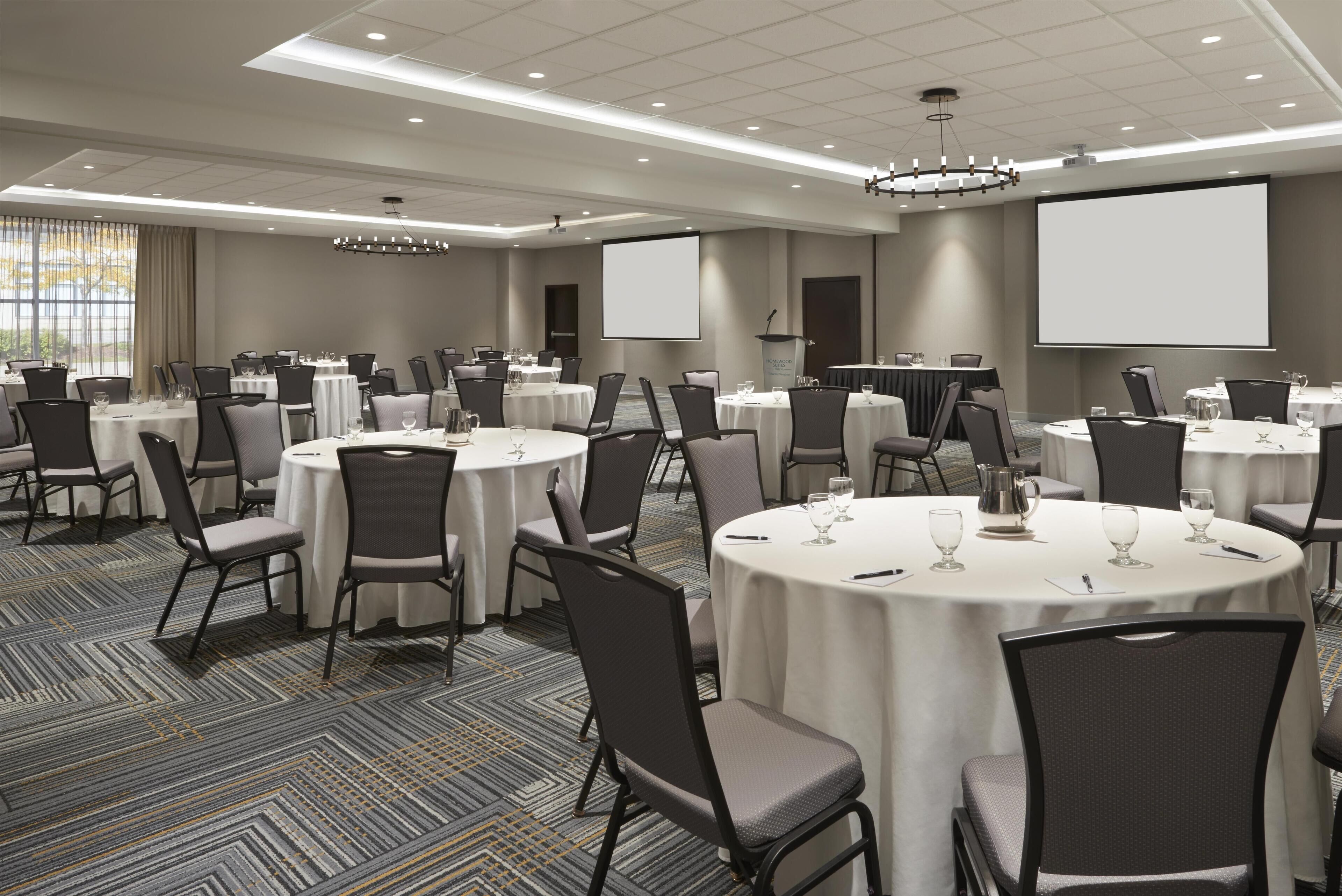 A conference room with multiple round tables, chairs, and a large screen.
