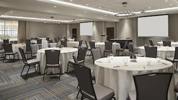 A conference room with multiple round tables, chairs, and a large screen.