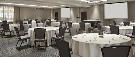 A conference room with multiple round tables, chairs, and a large screen.