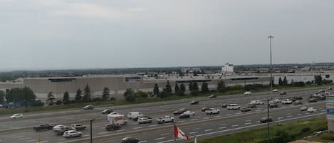 A highway with multiple lanes and vehicles, including cars and trucks. There are industrial buildings and a large warehouse in the background.