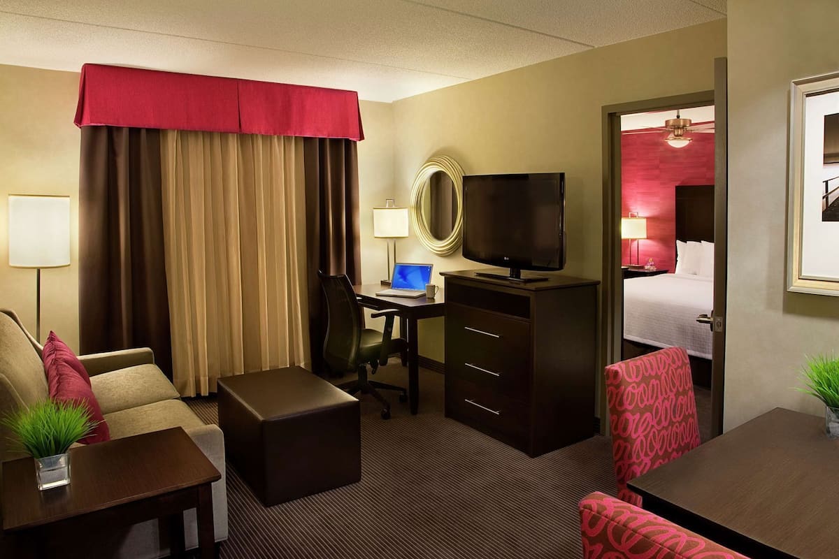 A hotel room with a bed, desk, chair, TV, and a small table with a plant.