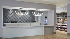 A hotel reception area with a modern design, featuring a reception desk, a minibar, and a 'Suite Shop' with various items on display. - Homewood Suites by Hilton Toronto Vaughan (Vaughan)