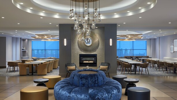 A spacious lounge area with a central seating arrangement, multiple tables, and a fireplace. - Homewood Suites by Hilton Toronto Vaughan (Vaughan)
