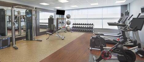 A gym with cardio machines, weightlifting equipment, and dumbbells.