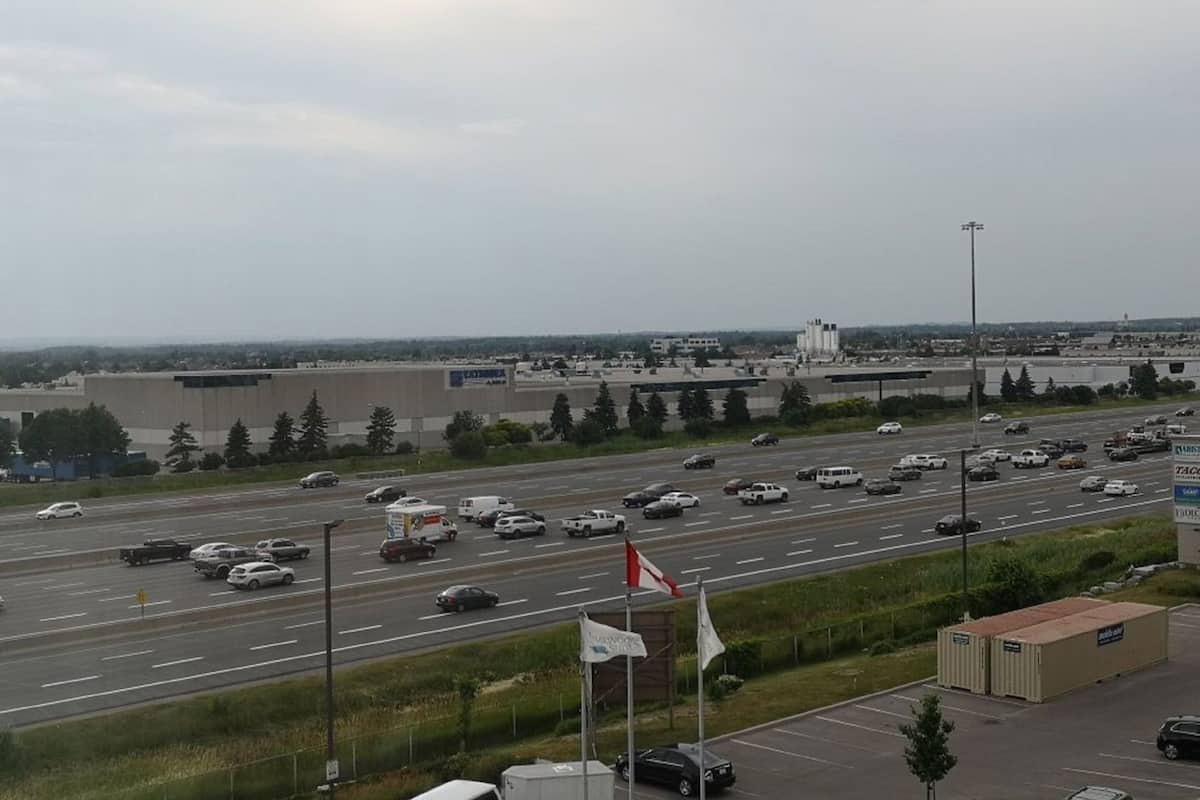 A highway with multiple lanes and vehicles, a large industrial building in the background, and a flagpole with flags.