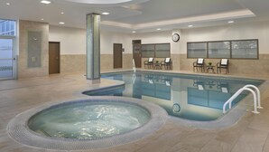 A modern indoor pool area with a hot tub, seating by the pool, and a clock on the wall. - Homewood Suites by Hilton Toronto Vaughan (Vaughan)