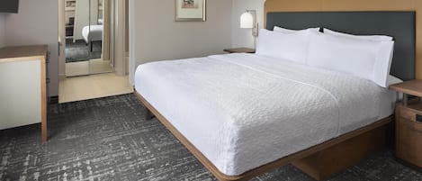 Ett hotellrum med en stor säng, ett skrivbord, en stol, ett nattduksbord och en inramad tavla på väggen.