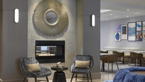 A modern interior with two grey armchairs, a black fireplace, and a large mirror on the wall. - Homewood Suites by Hilton Toronto Vaughan (Vaughan)