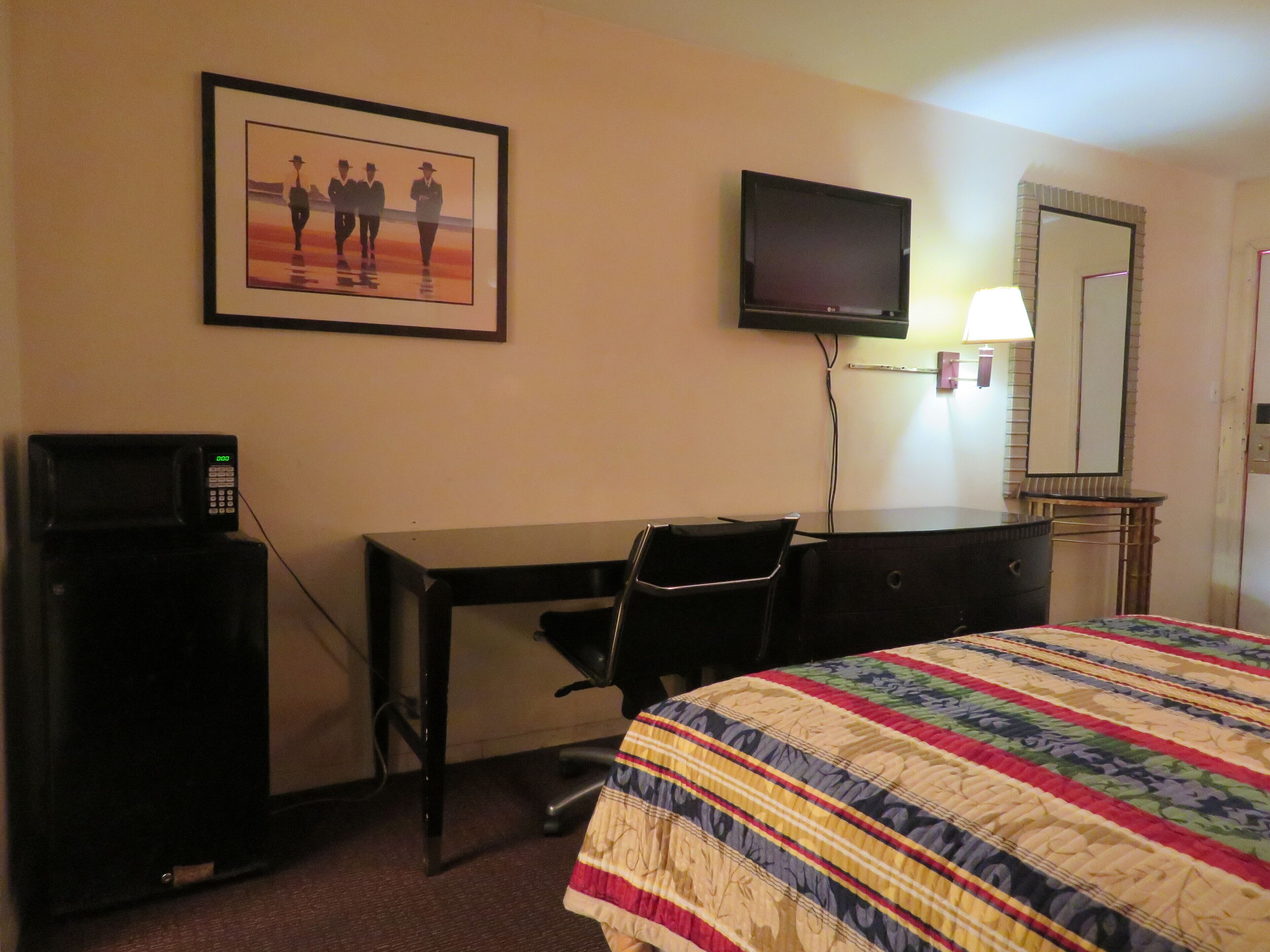 A hotel room with a bed, a desk with a chair, a television, a microwave, and a framed picture on the wall.