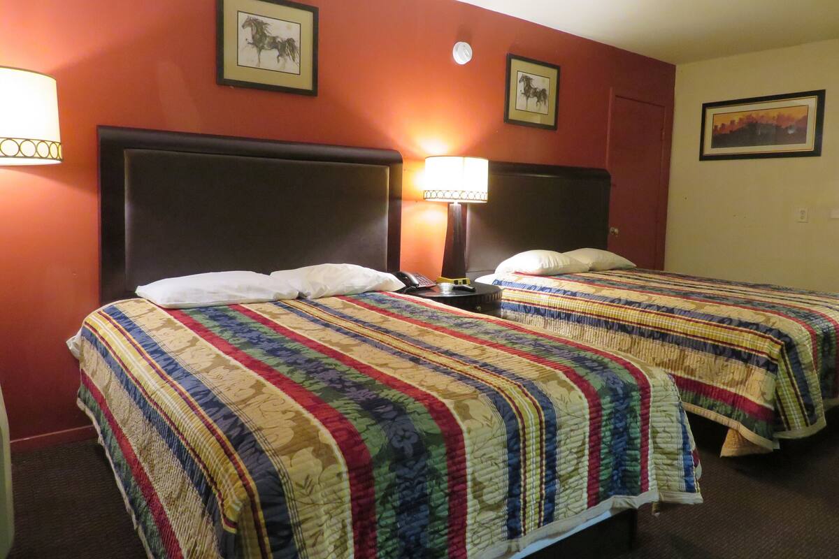 A hotel room with two beds, each with a colorful quilt, a nightstand with a lamp, and framed pictures on the walls.