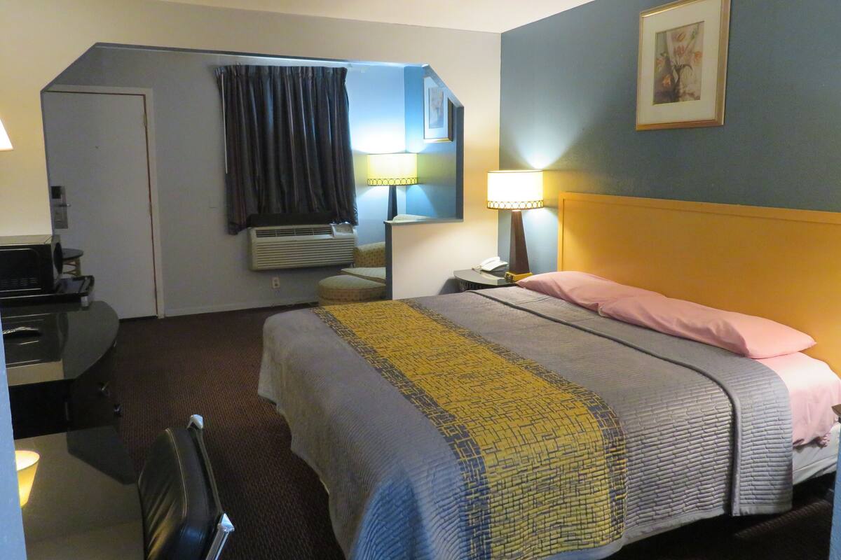 A hotel room with a bed, bedside lamp, air conditioning unit, and a desk with a telephone.