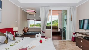 A hotel room with a bed, a TV, a desk, and a view of a balcony and outside scenery.