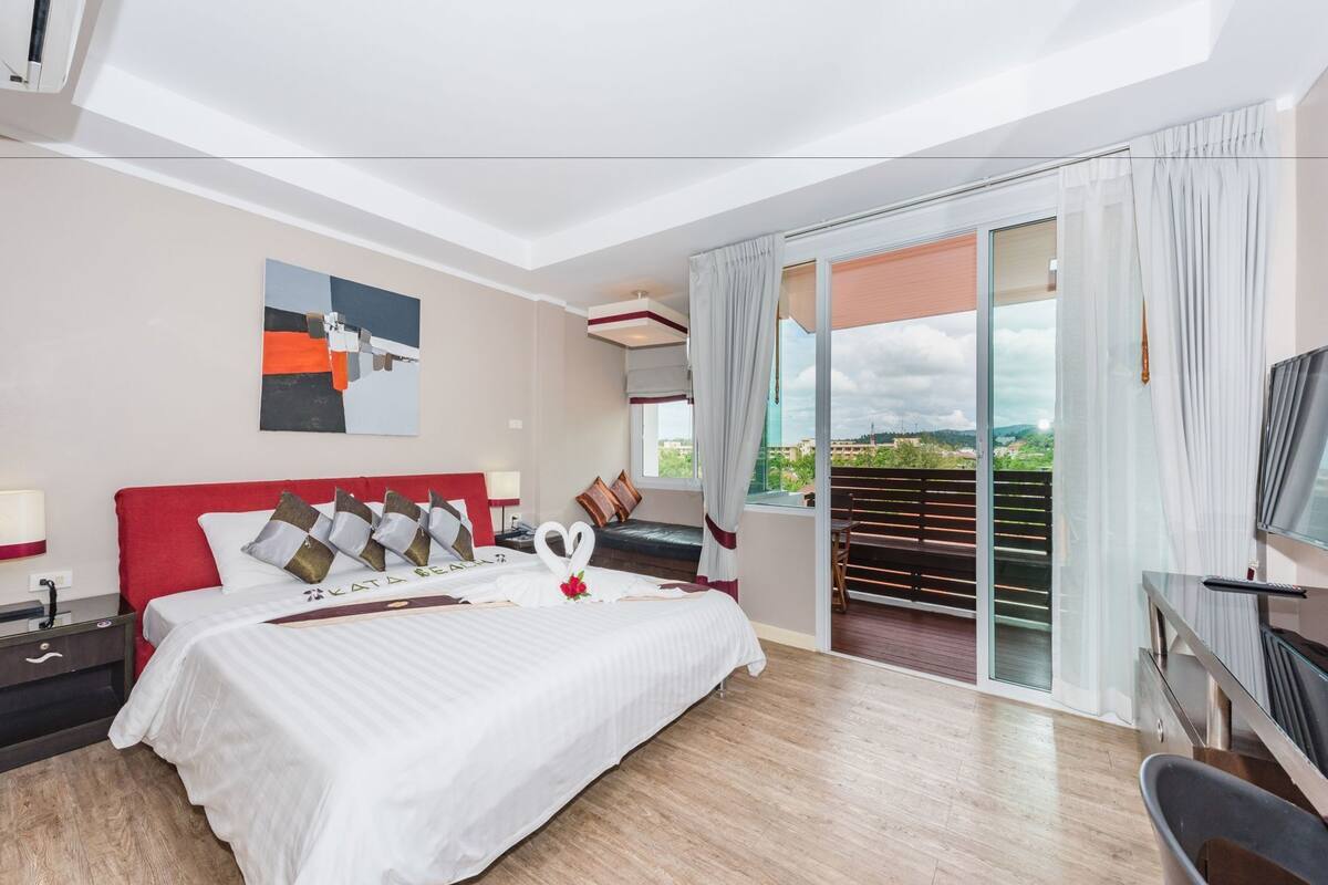 A hotel room with a bed, a desk, a TV, and a balcony with a view.