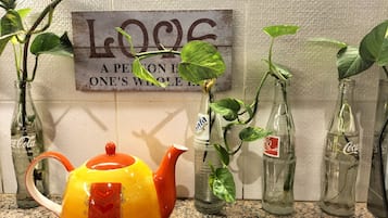 A kitchen counter with a yellow teapot, Coca-Cola bottles repurposed as planters, and a sign with the text "A PERSON IS ONE'S WHOLE BODY".