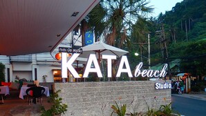 A sign for KATA Beach Studio with outdoor seating and palm trees in the background.