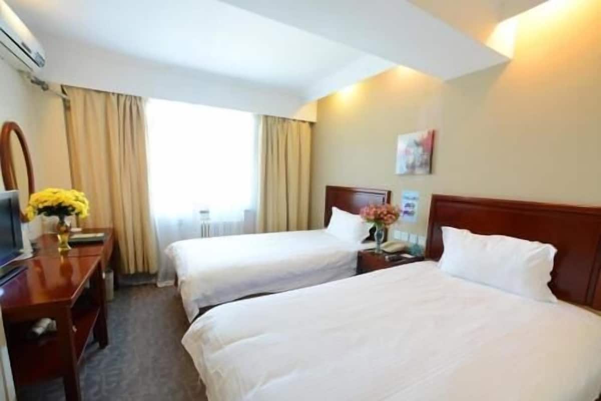 A hotel room with two beds, a desk, a chair, a TV, and a window with curtains.