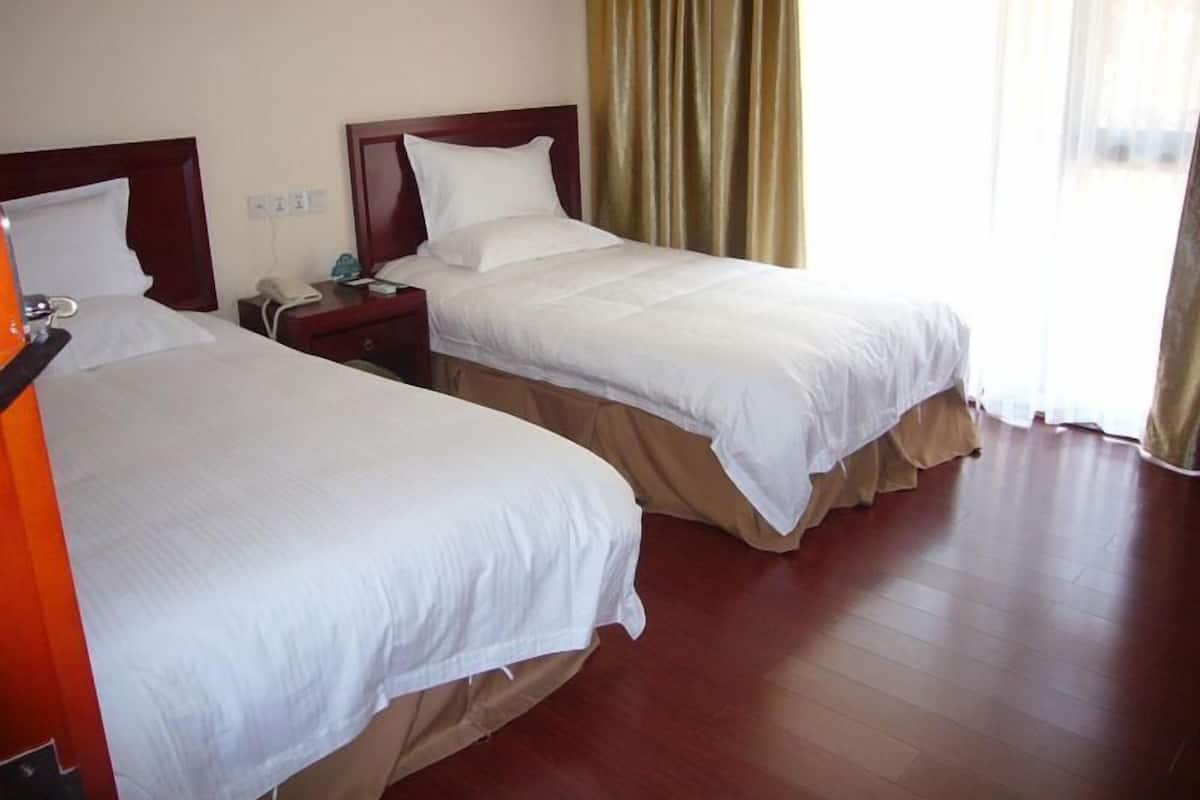 Two single beds with wooden headboards, a bedside table with a lamp, and a window with curtains.